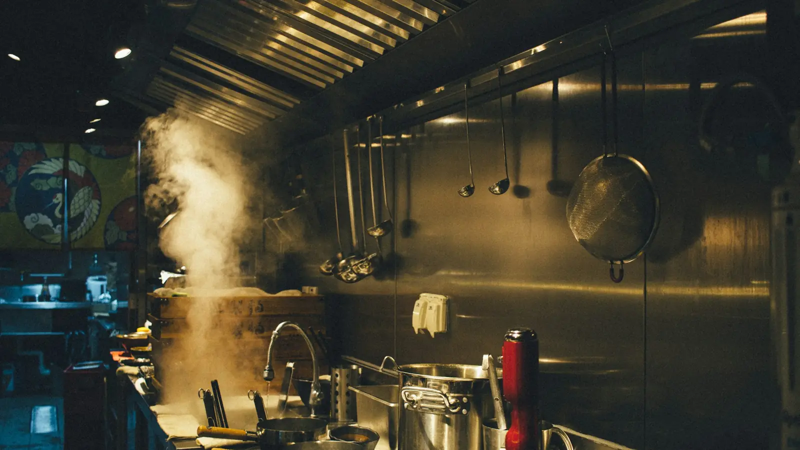 Professionele restaurantkeuken met stomende pannen op het fornuis onder een roestvrijstalen afzuigkap